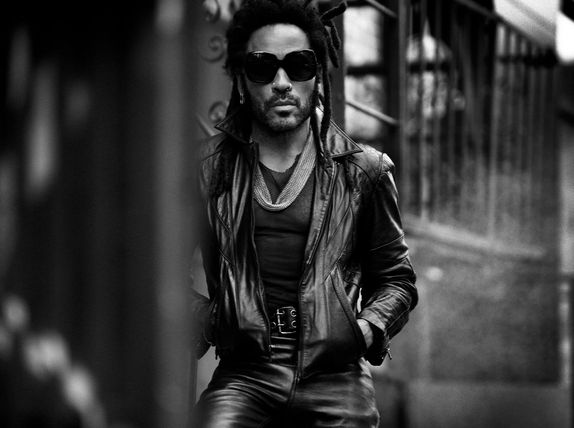 Lenny Kravitz wearing leather jacket and pants staring into the camera with sunglasses in a city.