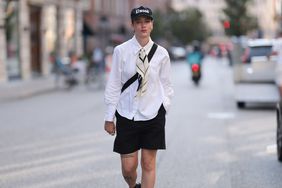 Person wearing a black hat, white button down, black shorts, and a bandana as an ascot