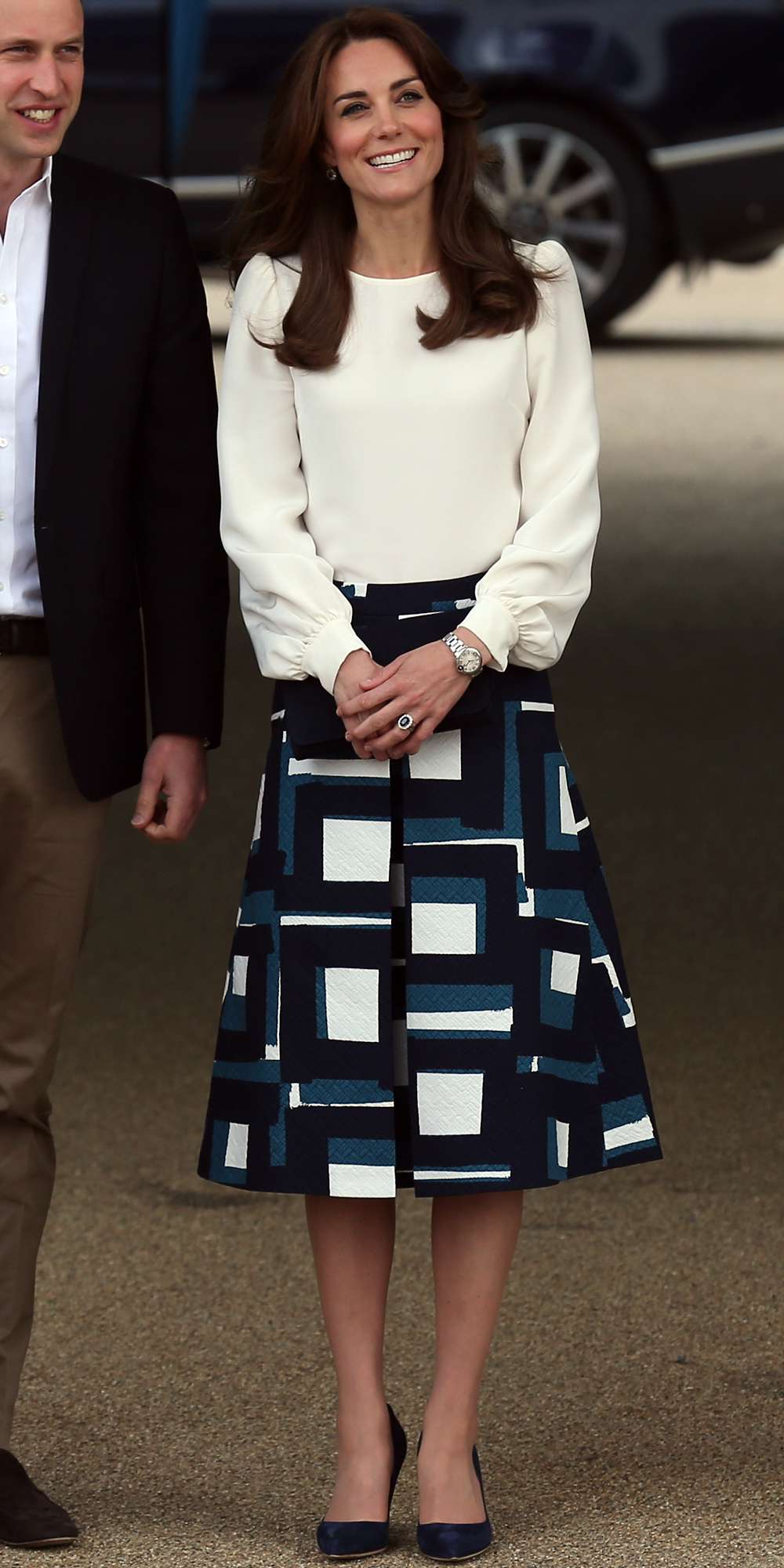 Kate Middleton in a cream blouse, patterned Banana Republic skirt, and navy heels