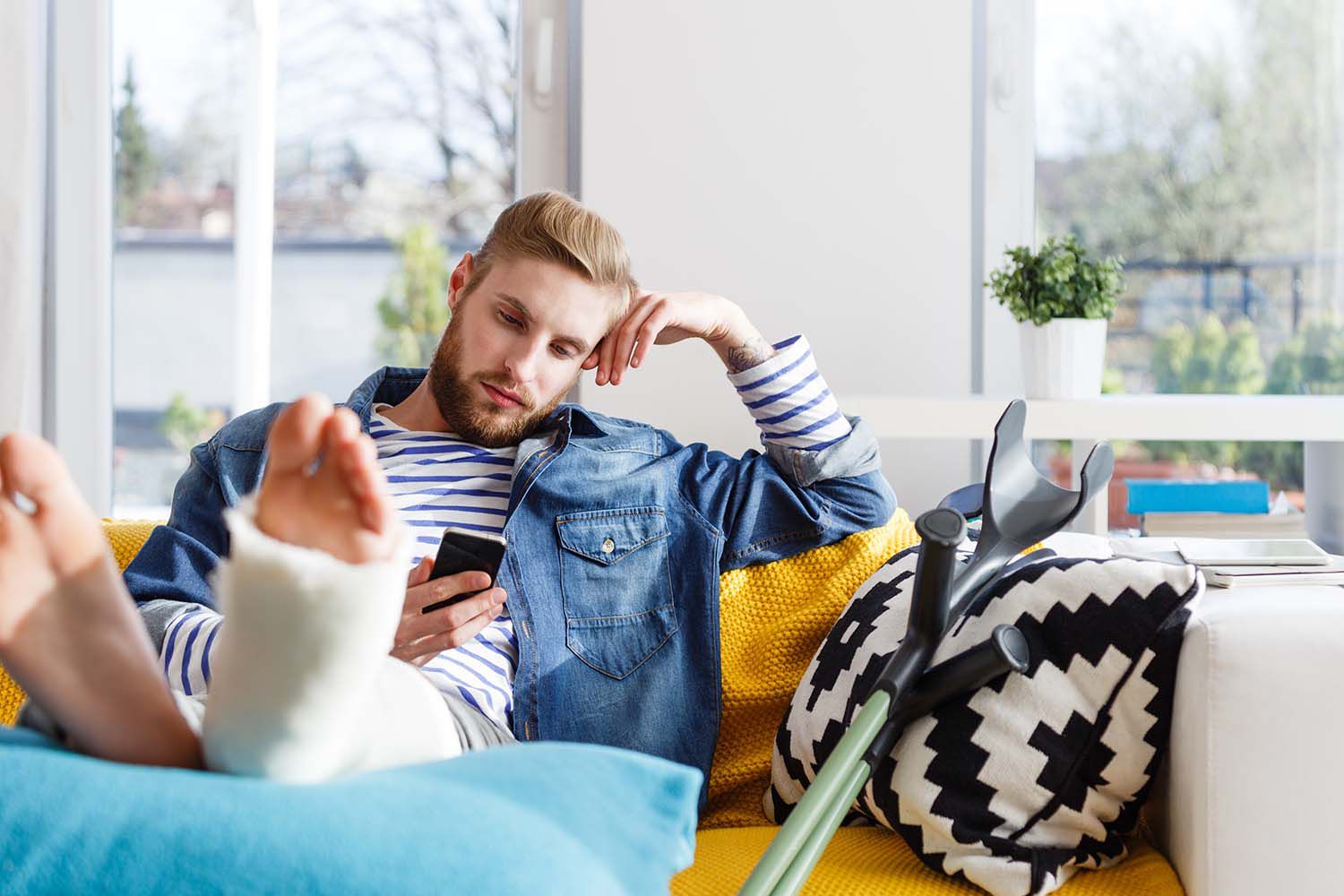 Young man with broken leg using smart phone at home