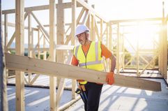 Construction worker carries a beam while working on an unfinished wooden structure
