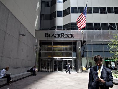 A man looks at his phone outside the headquarters of BlackRock Inc., which displays the company name beside an American flag.