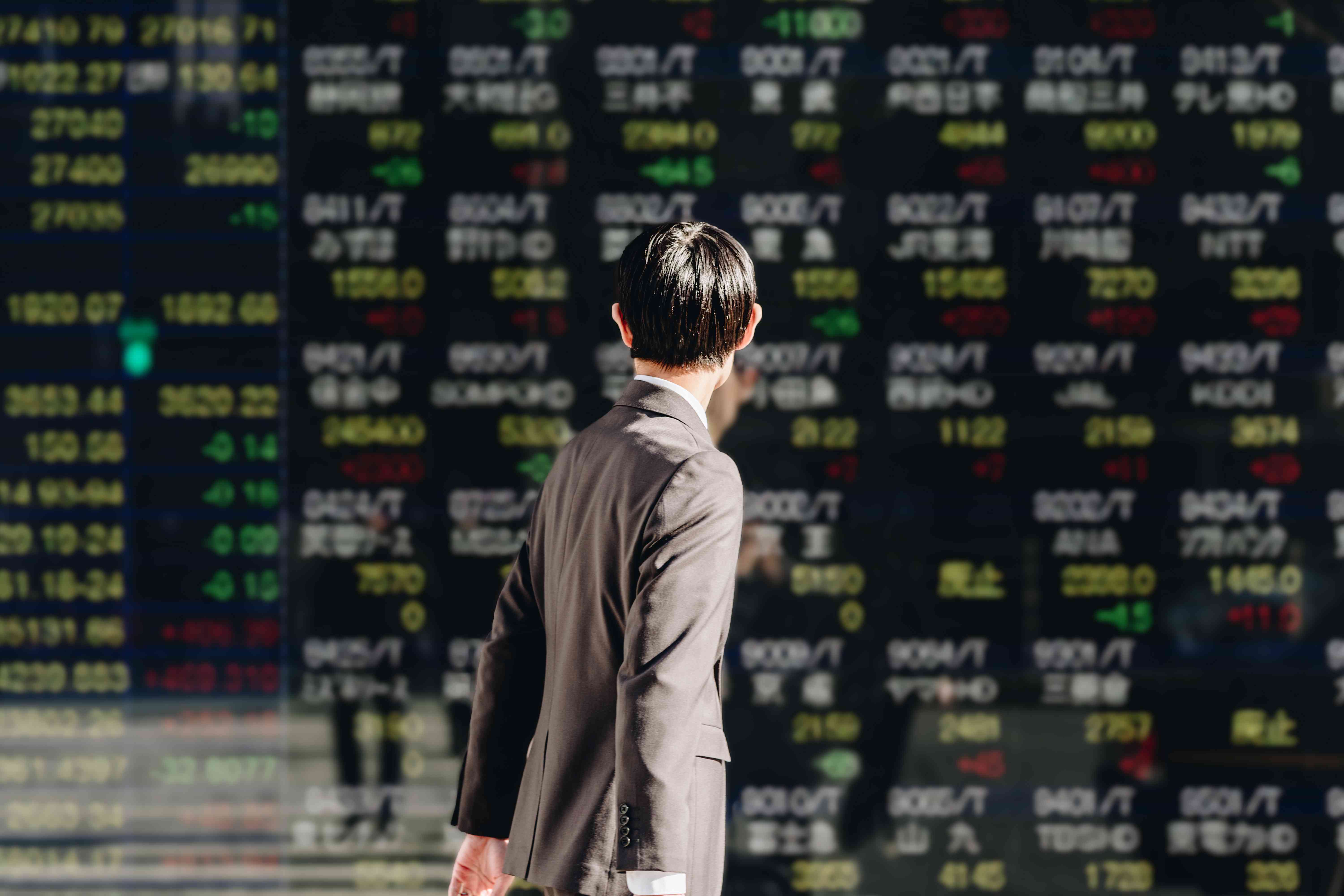 Person walking by a Japanese stock price board