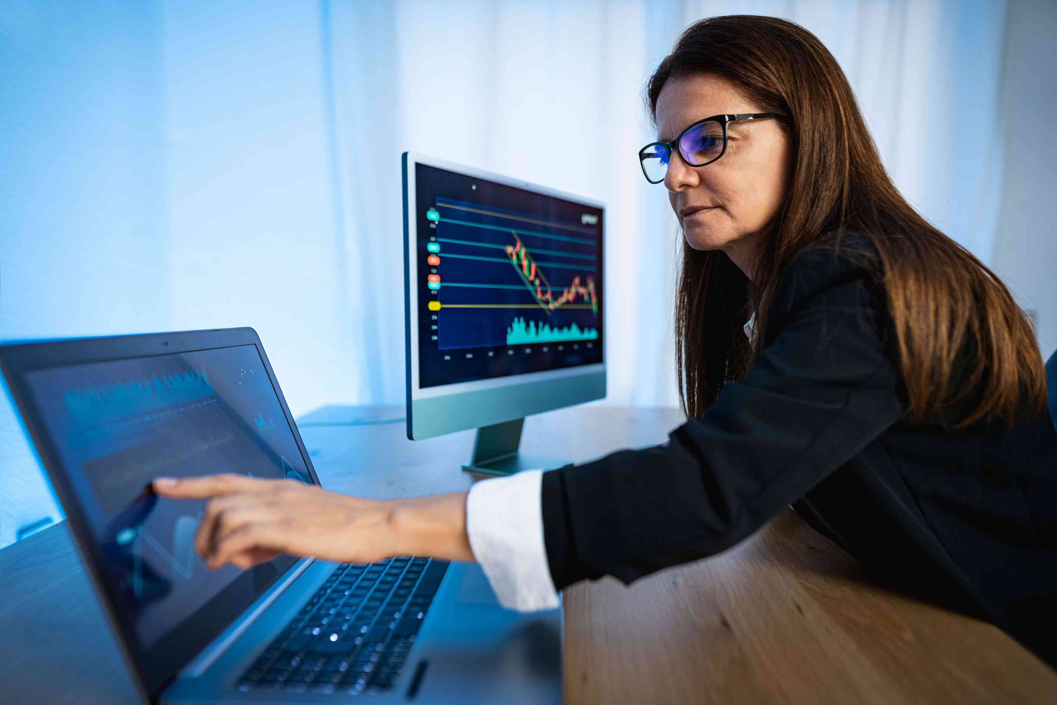 Woman looking at two computer screens with market trading information displayed