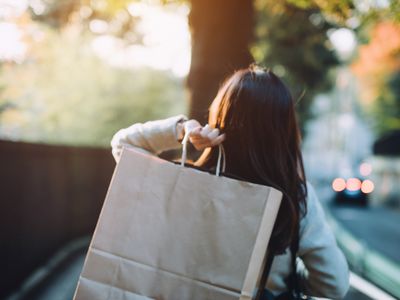 Rear view of woman carrying shopping bag over shoulder walking on city street