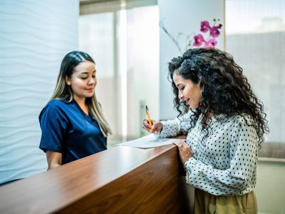 Woman talks with receptionist at dentistâs office reception desk