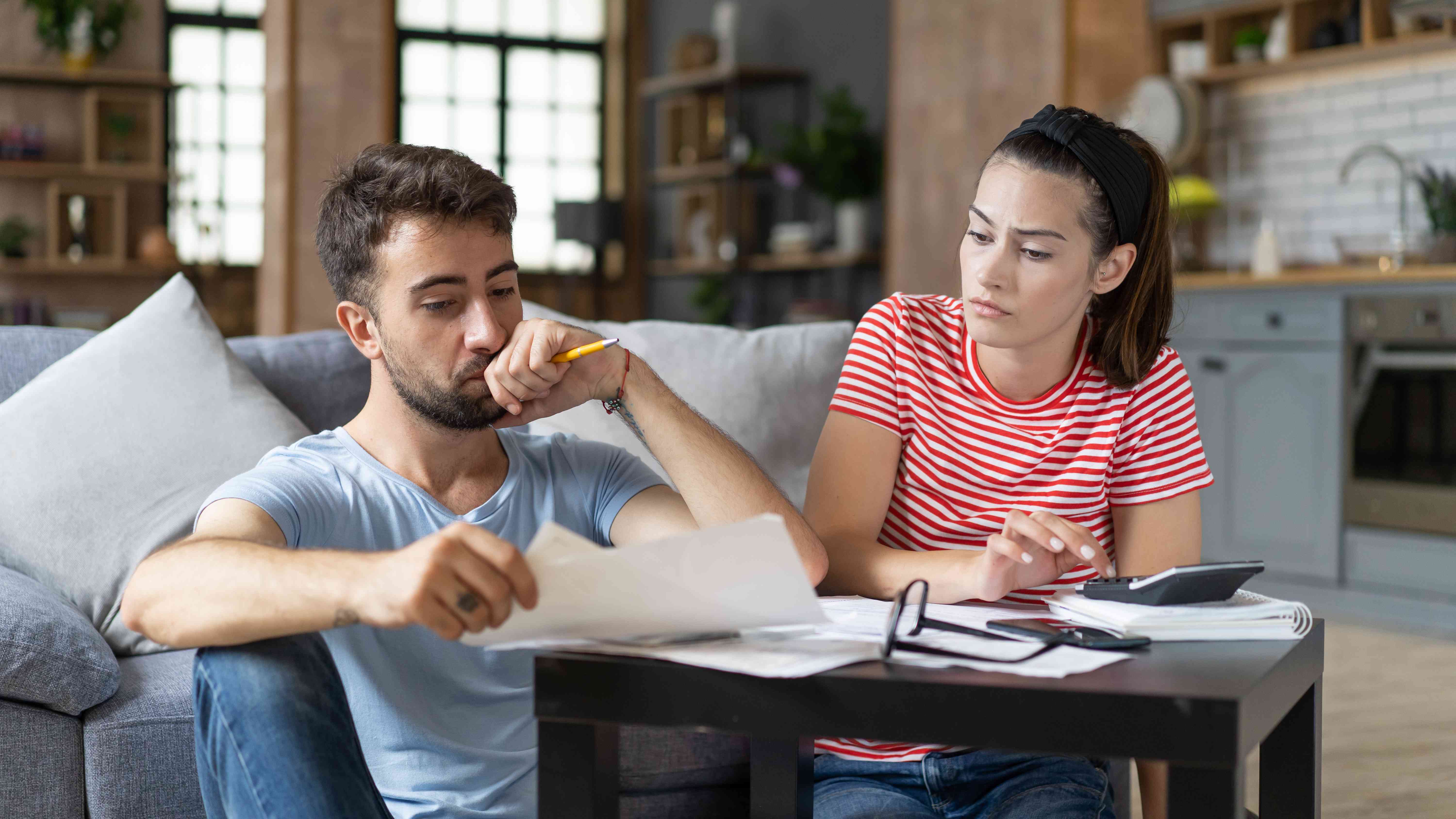 Young couple at home looking concerned as they review papers and use a calculator