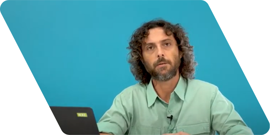 Homem branco de cabelos castanhos enrolados até a altura dos ombros e barba olhando para a câmera. Ele usa uma camisa de cor verde clara e está na frente de uma parede azul.