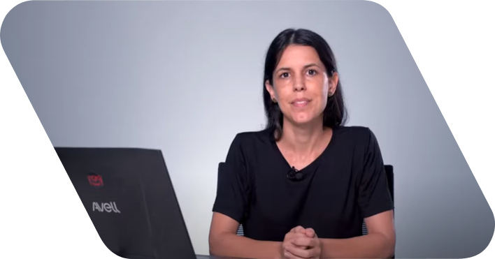 Mulher de cabelo longo e liso vestindo uma camisa preta. Ela fala para câmera em frente a um fundo cinza.