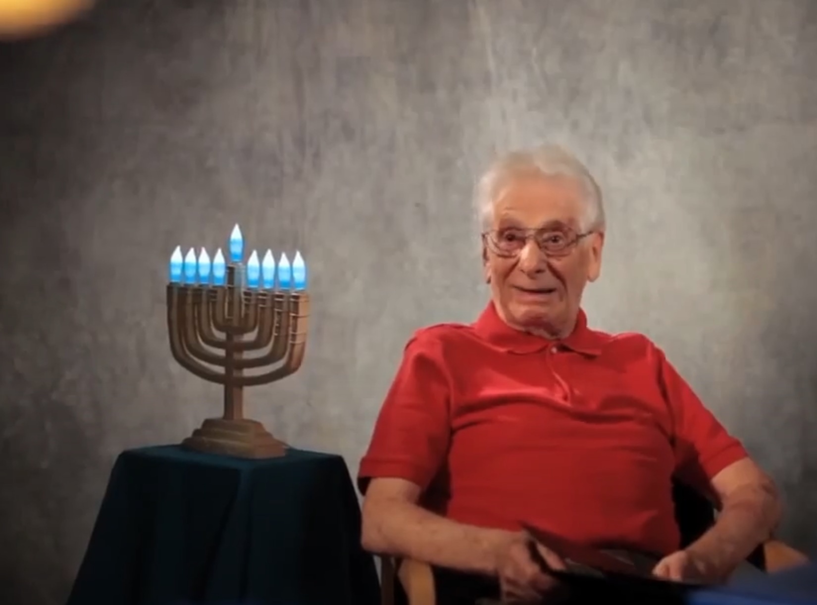 Smiling older man sitting by a Menorah