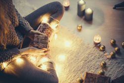 Woman sitting with Christmas present and fairy lights on the carpet