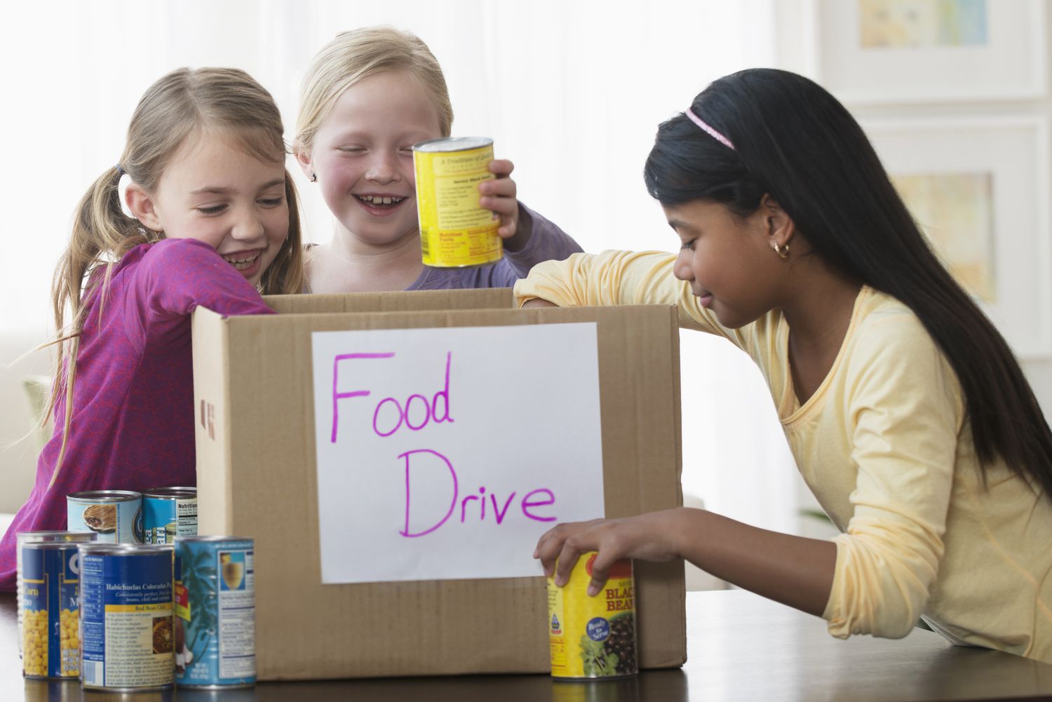 Girls placing cans of food in donation box