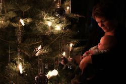 Mother Holding Cute Baby Boy Against Christmas Tree At Night