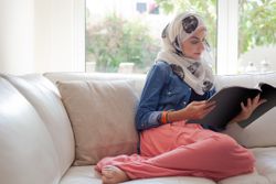 Arab woman reading a magazine on the sofa.