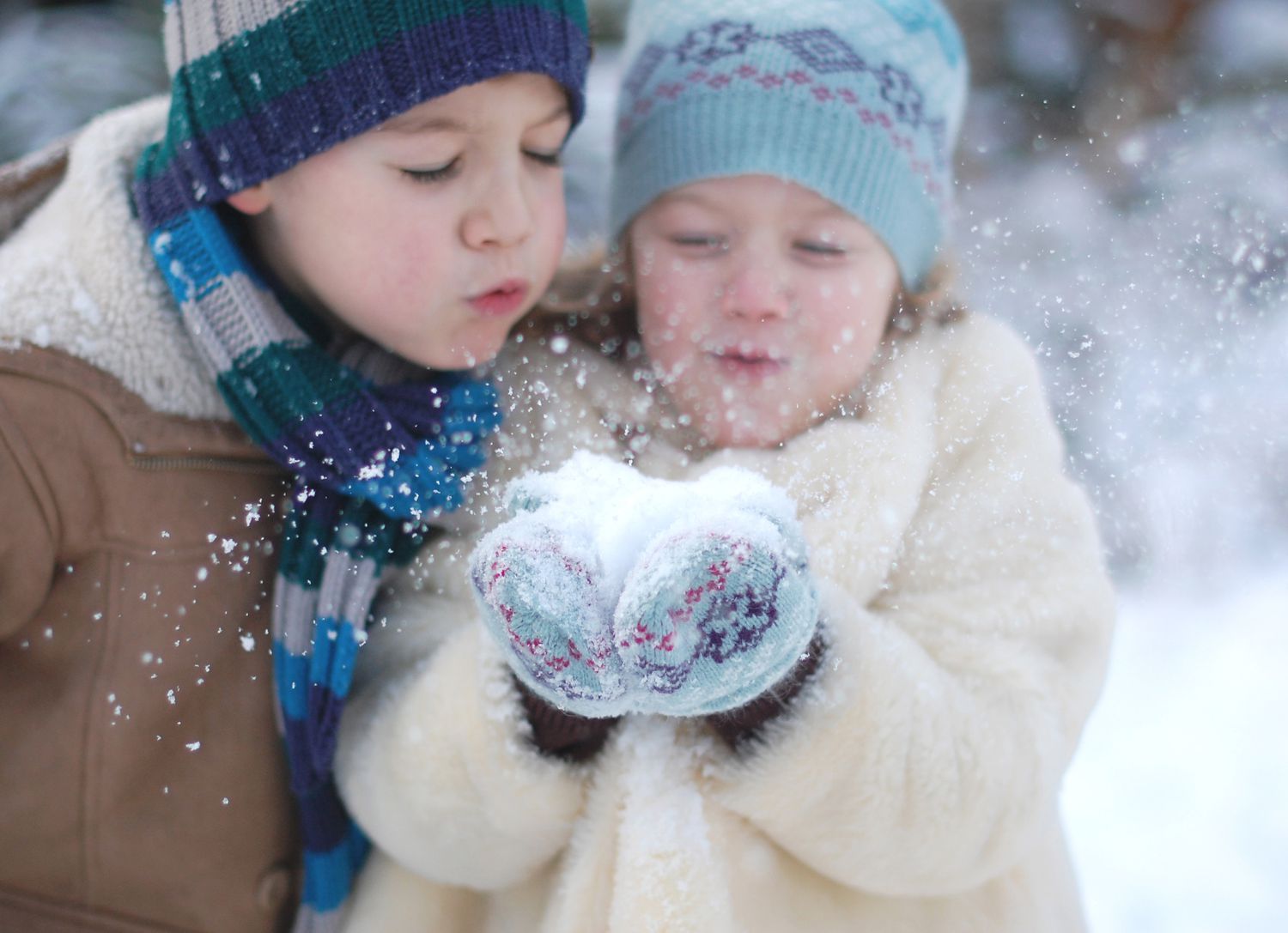 A brother and sister blowing snow towards the camera.