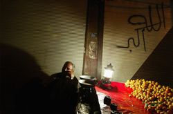 A man sells fruits past midnight under a graffiti saying 'Allahu Akbar -god is Great'