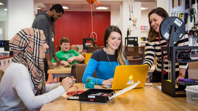 Happy students at a big table with a laptop and electronics kit