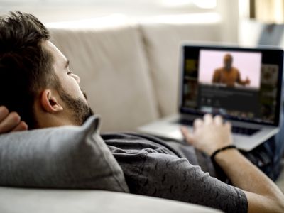 A man lying down on a couch watching Mad Max: Fury Road on Netflix on a laptop.