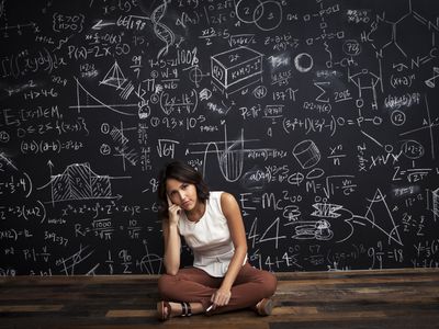 Person sitting cross-legged in front of chalkboard full of mathematical equations