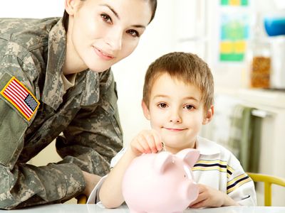 Female soldier with son dropping coins into pink piggy bank.