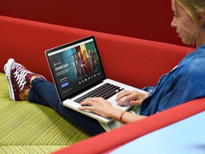 A person watching Discovery Plus on a laptop while lounging on a couch. 