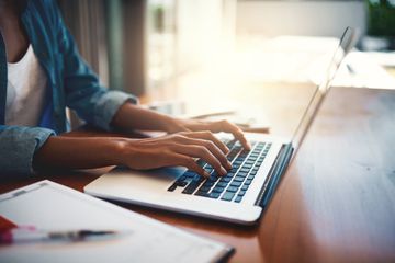 A woman sitting at a desk using a MacBook laptop.