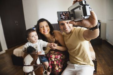 A man holding a camcorder towards himself and his family.