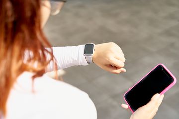 A woman holding an iPhone and looking at her Apple Watch