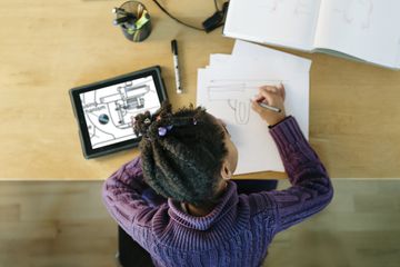 Child learning online with tablet and paper and pencil.