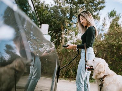 Asian woman charging her car and holding leash for Golden Retriever.