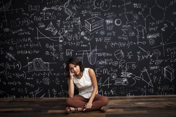 Person sitting cross-legged in front of chalkboard full of mathematical equations