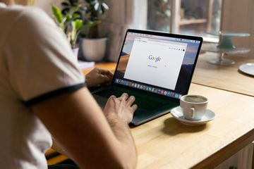 Human using computer running google chrome with an cup of coffee close to the keyboard.