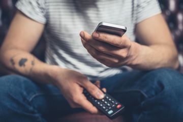 Person holding iPhone and television remote