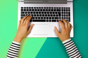 Cropped hands of woman using laptop over colored background