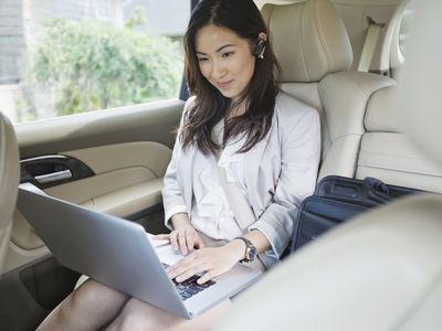 Woman using laptop in car with Bluetooth headset