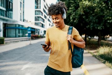 A man wearing a yellow T-shirt and headphones listening to an Apple Music playlist on a black iPhone.