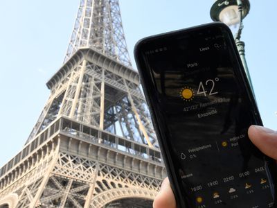 A person standing next to the Eiffel Tower holds a smartphone