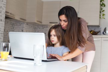 Cute girl and mother using laptop at home