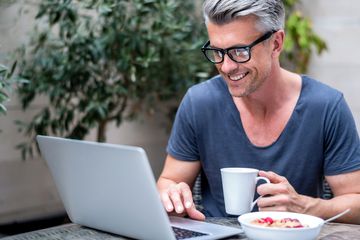 Man wearing glasses using an internet browser on his laptop in a cafe.