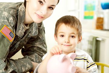 Female soldier with son dropping coins into pink piggy bank.