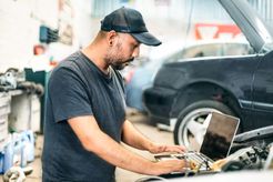 Auto technician with computer connected to car.