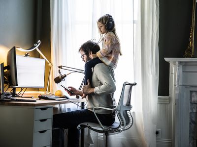 A parent working from home with their child sitting on their shoulders.