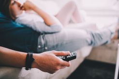 A couple snuggled together on the couch watch TV with the remote of the tv in hand