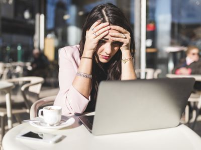 A remote worker looking frustrated while sitting at a cafe with a laptop computer open.