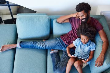 A father and daughter sitting on a couch using a tablet computer