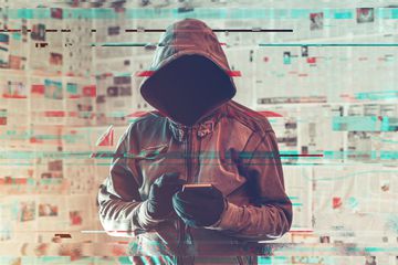 A hooded hacker person using a smartphone. 