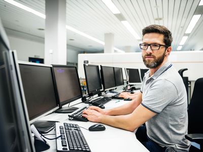 A man wearing classes and a polo shirt sitting at a computer desk in an office looking at several Lenovo monitors.