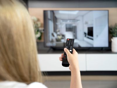 A blonde woman sitting on a couch pointing a remote control at her LG smart TV running the Netflix app.