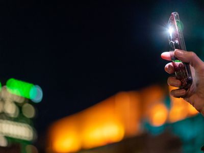 An iPhone with its flashlight illuminated. There's a blurred-out city in the background.