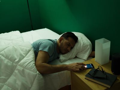 A man reaching for a smartphone on a bedside table